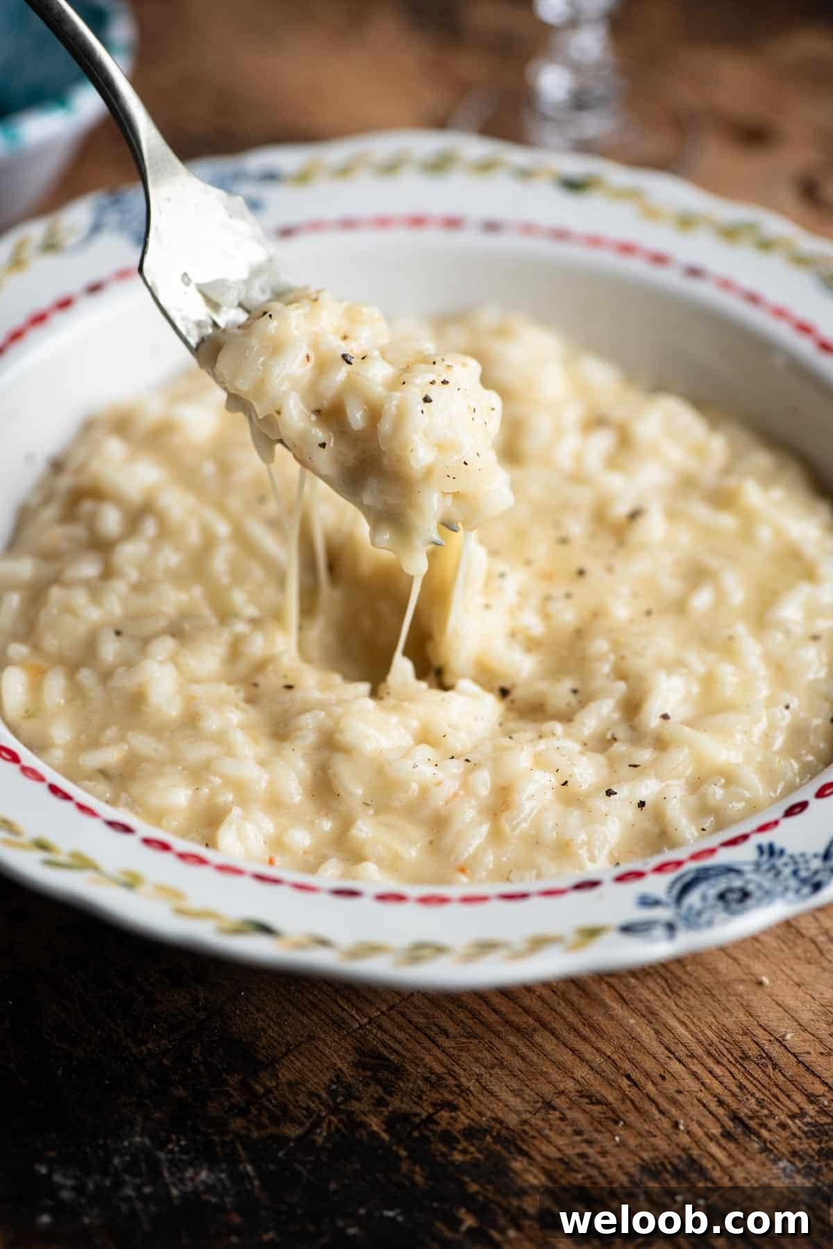A close up of a fork picking up cheesy risotto from a bowl.