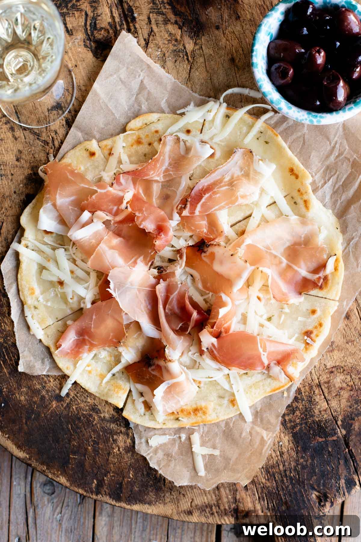 An overhead shot of Brustengo, an Italian flatbread topped with cured meat and cheese on a wooden board.