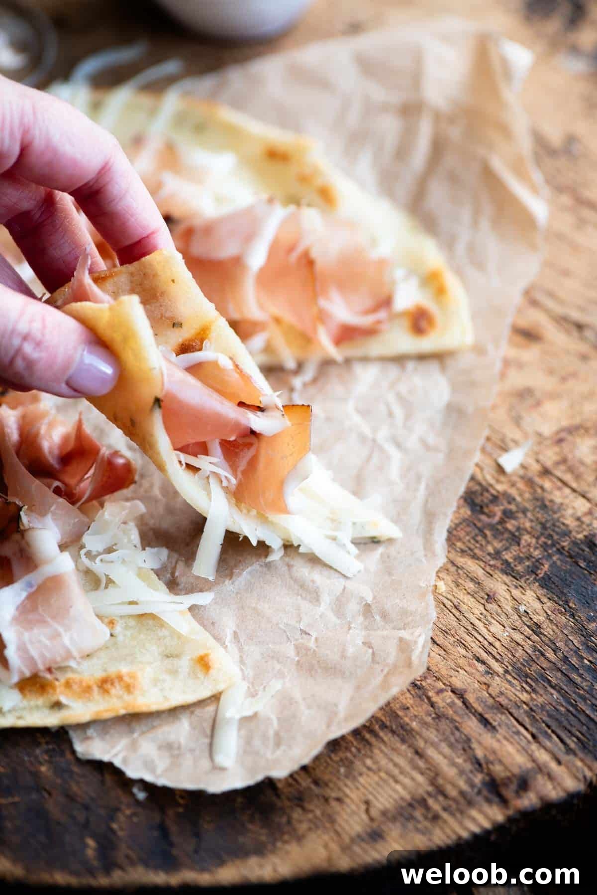 A hand picking up a slice of Italian flatbread topped with cured meat and cheese.