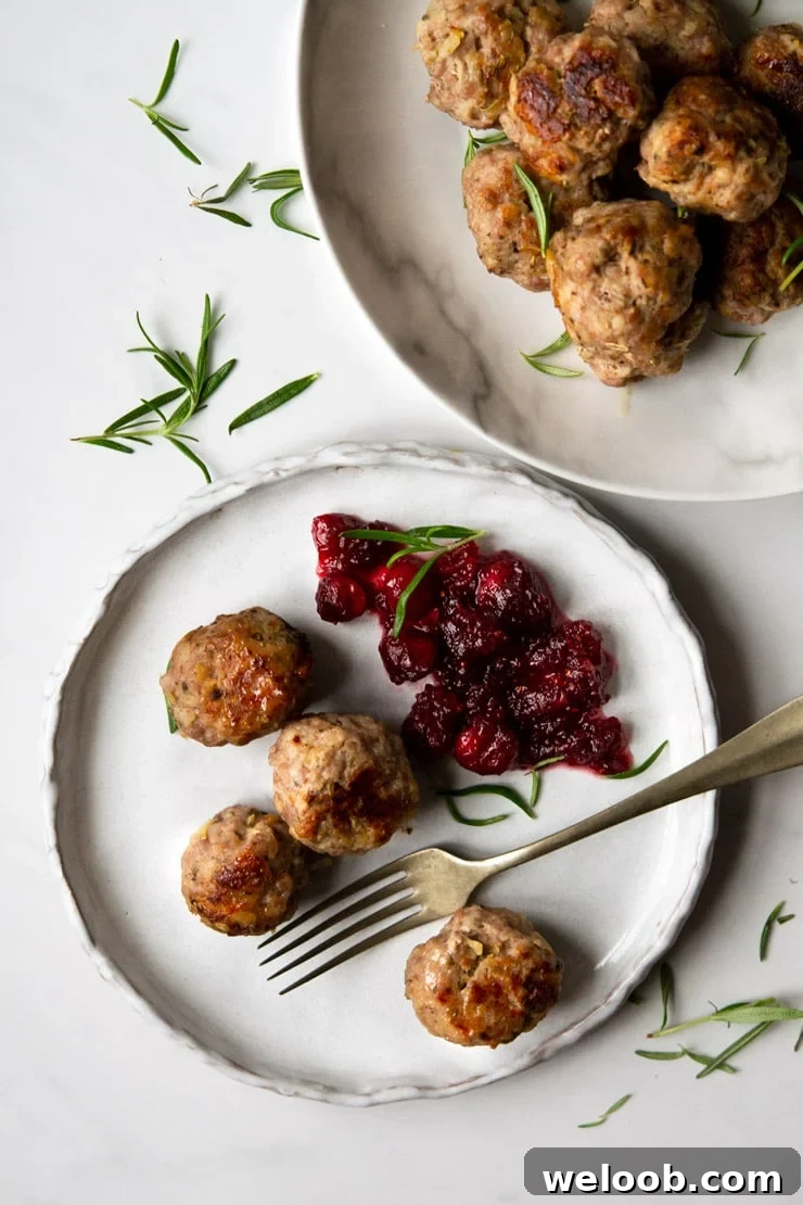 Sausage stuffing balls on a plate with cranberry sauce and fresh rosemary