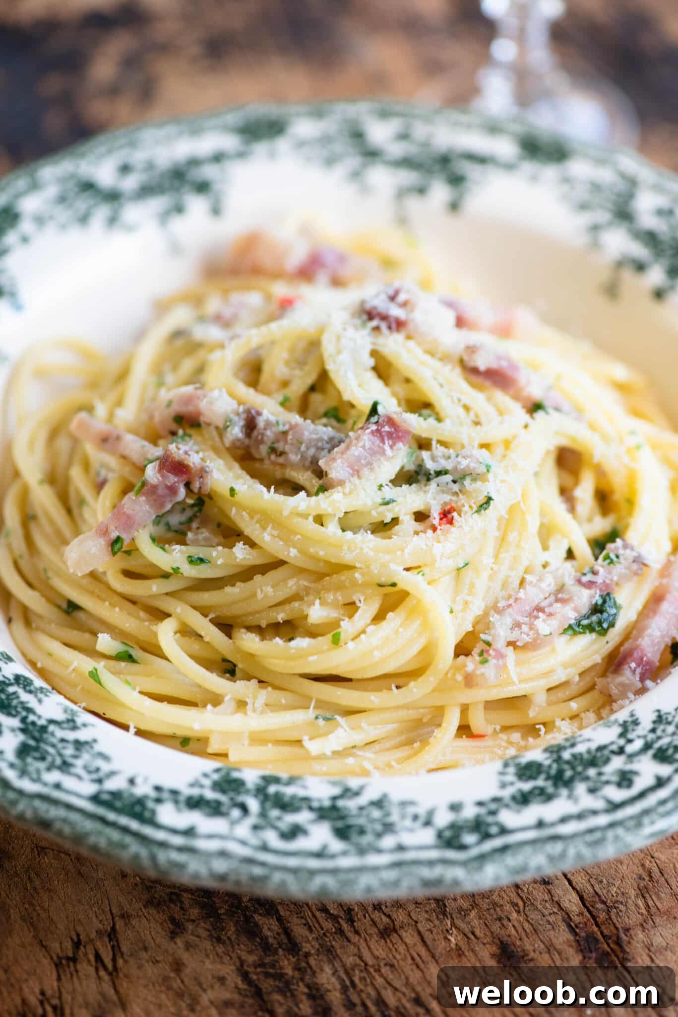 A close up of spaghetti topped with pancetta and onions in a green patterned bowl.