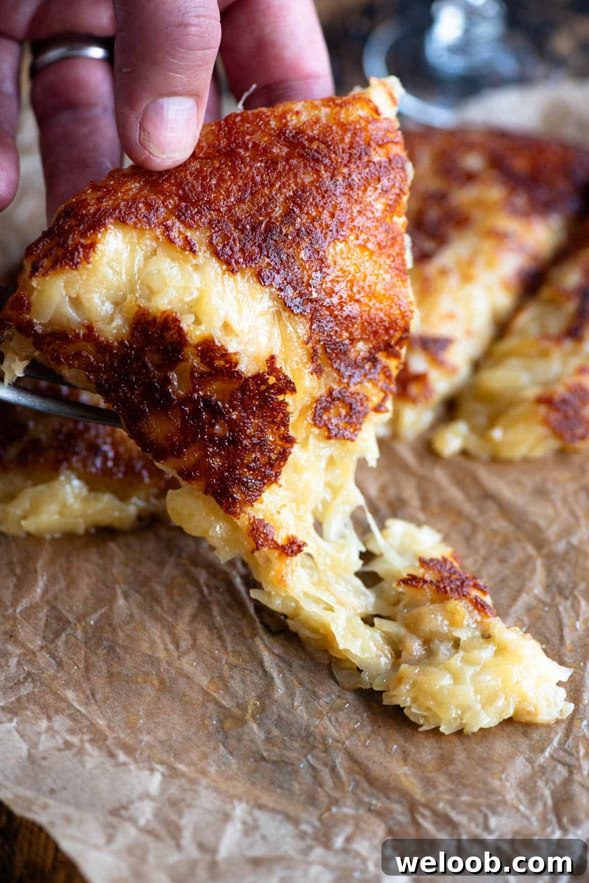 A hand picking up a slice of fried cheese and potato (frico) from a wooden board.