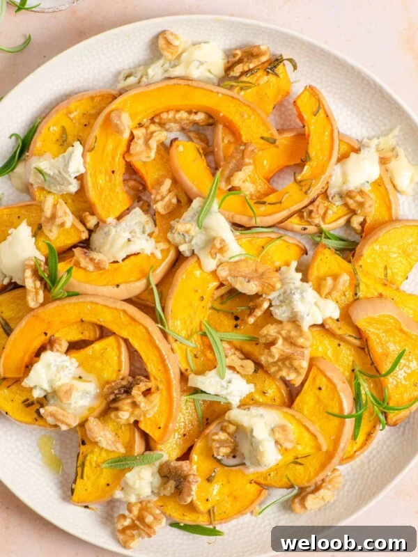 An overhead shot of roasted butternut squash on a serving plate with gorgonzola and walnuts