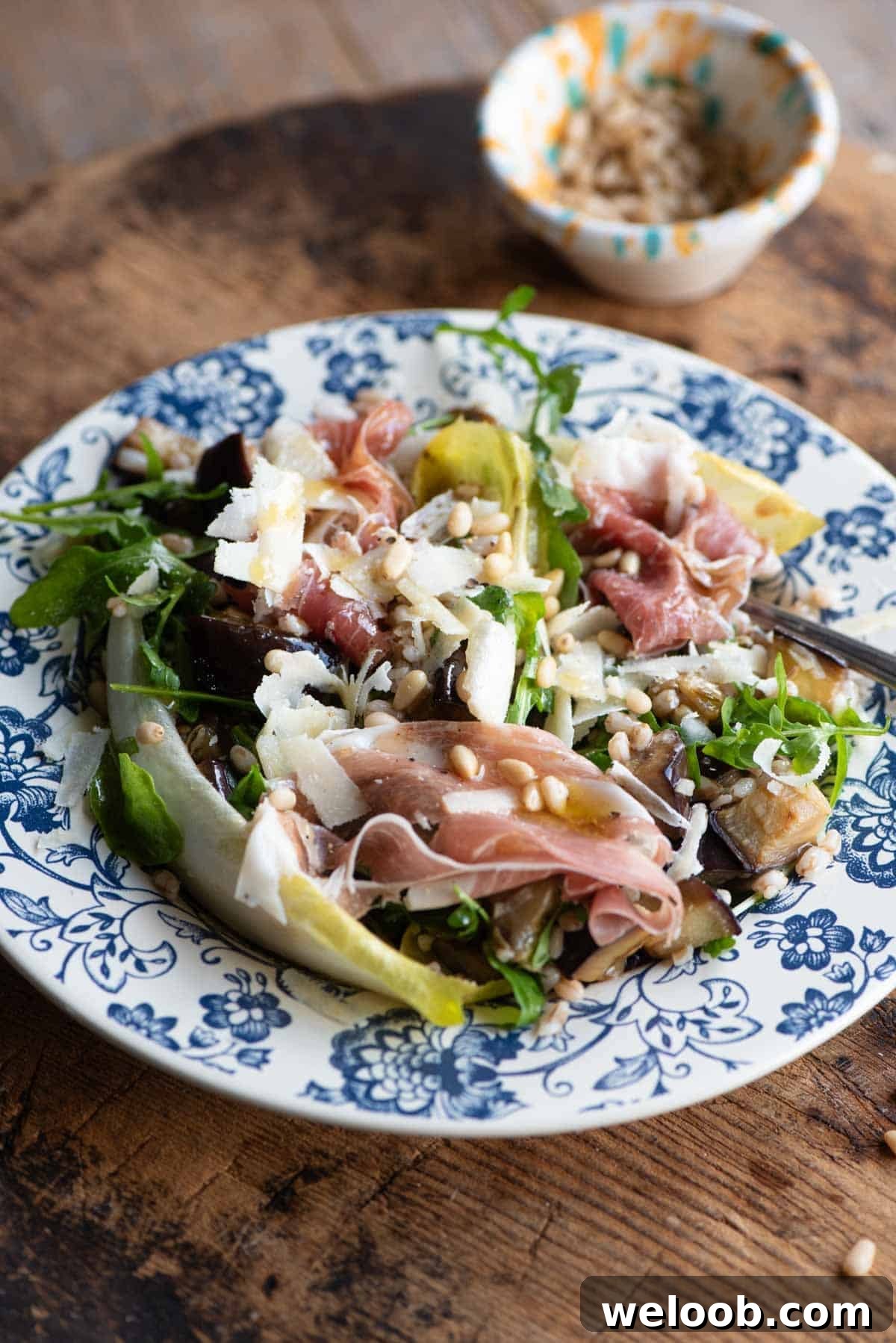 A close up of an eggplant and farro salad on a blue patterned plate on a wooden table.