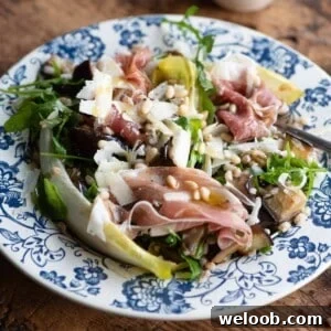 A close up cropped image of an eggplant and farro salad on a blue plate with prosciutto and pine nuts.