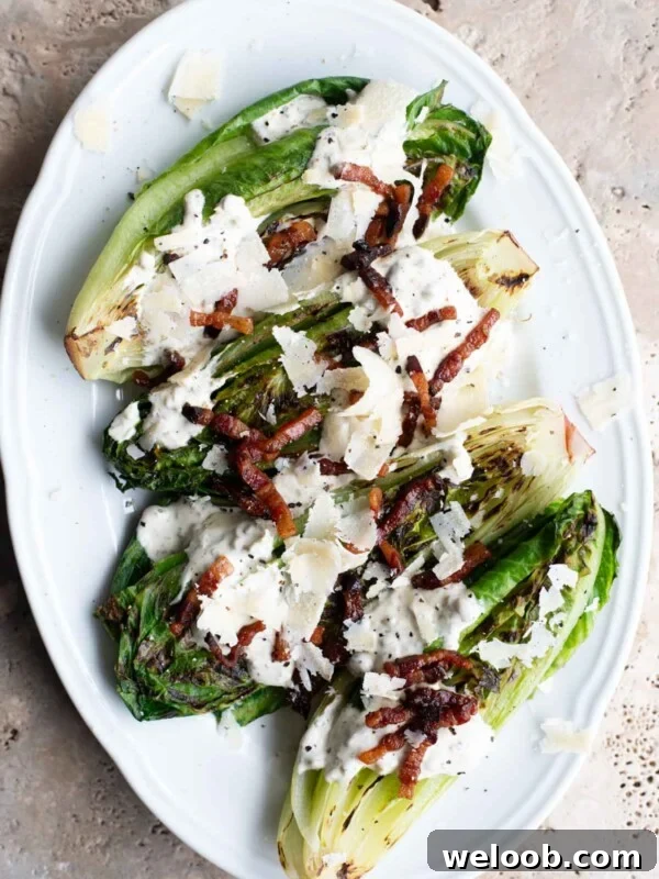An overhead shot of a white serving plate with grilled romaine lettuce topped with a creamy sauce, pancetta and Parmigiano Reggiano shavings.