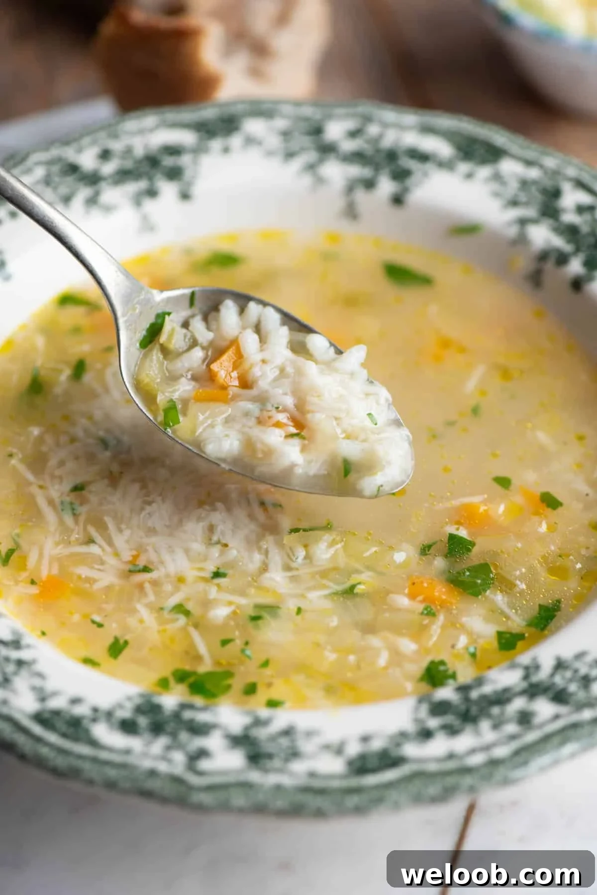 A close up of a spoon picking up a spoonful of Italian rice soup from a green patterned bowl.