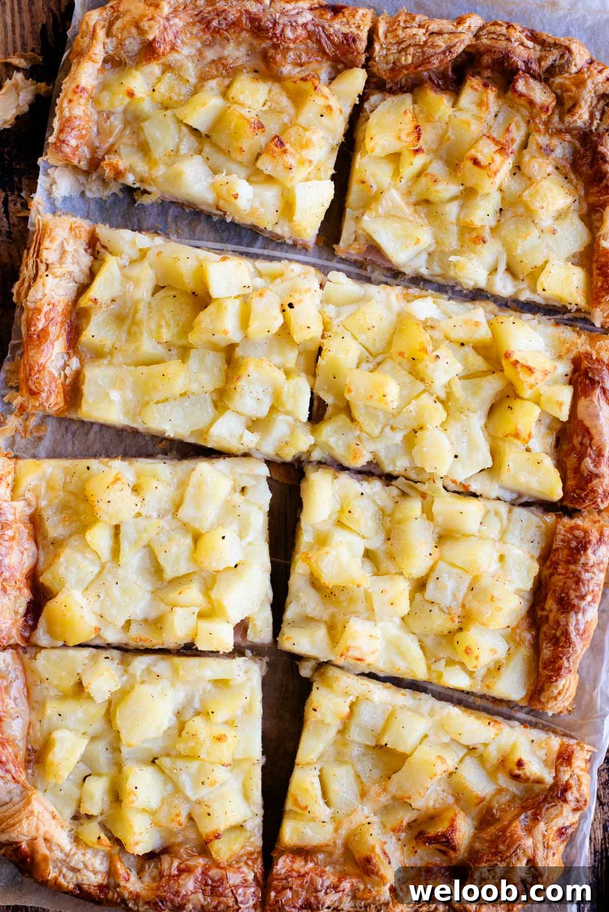 An overhead shot of a puff pastry tart topped with potatoes, ham and cheese and cut into 8 slices.