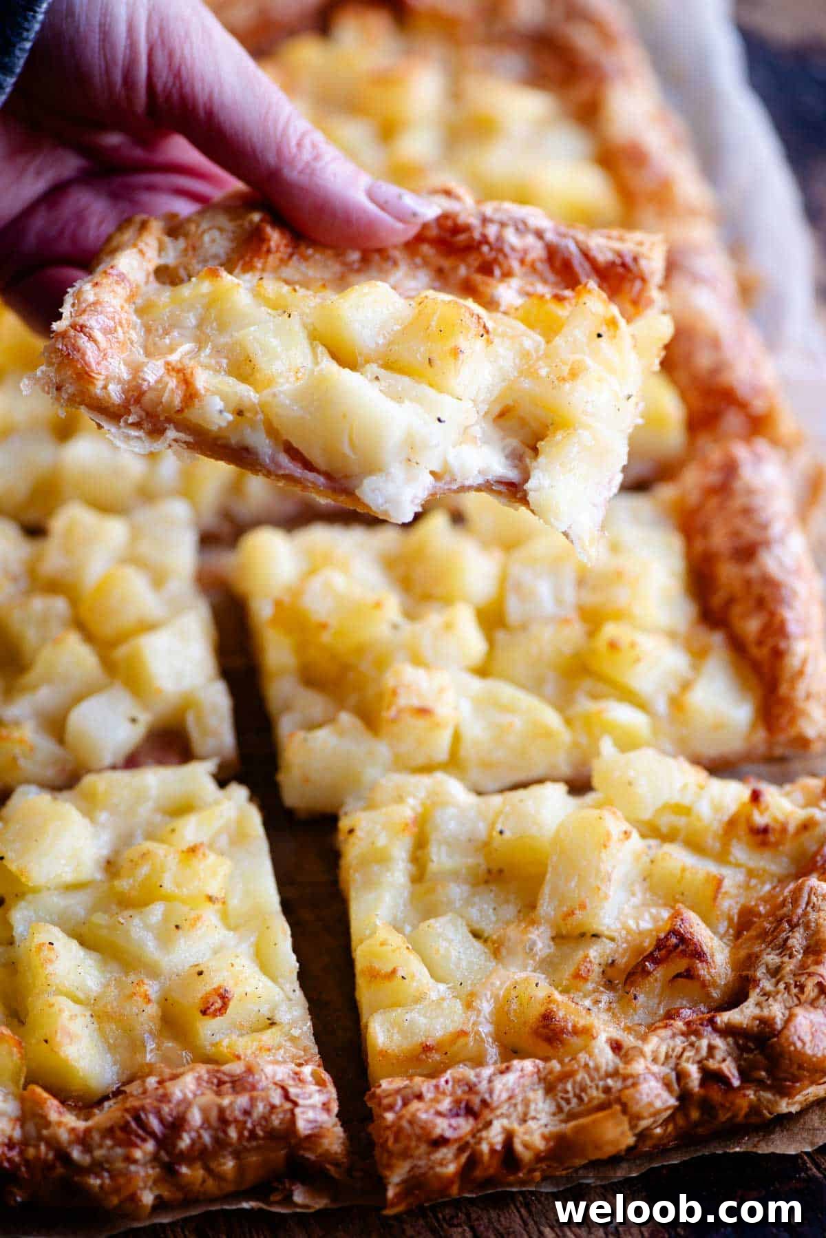 A close up of a hand holding a slice of puff pastry and potato tart.