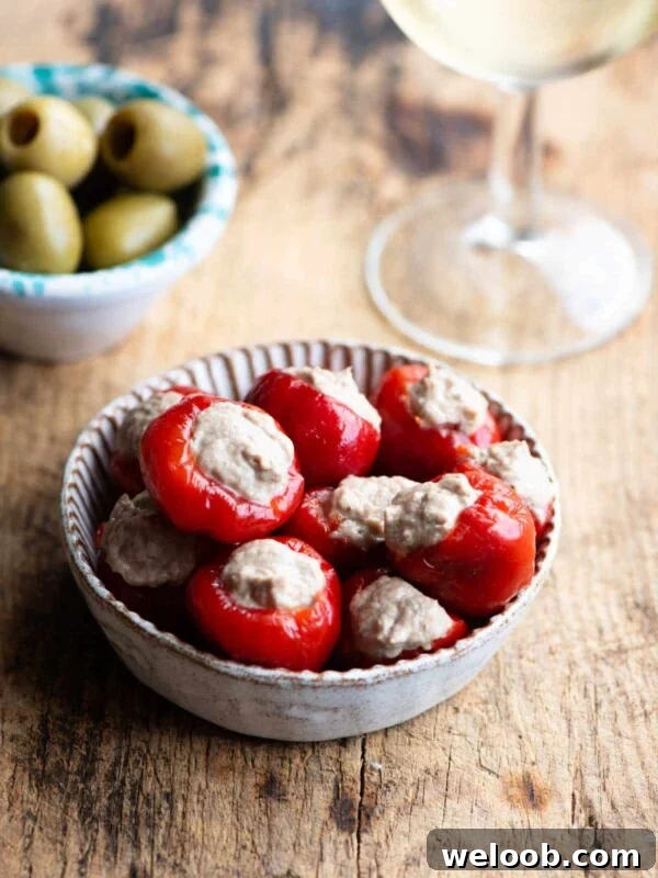 Tuna stuffed cherry peppers in a small dish with olives and a glass of wine at the side.