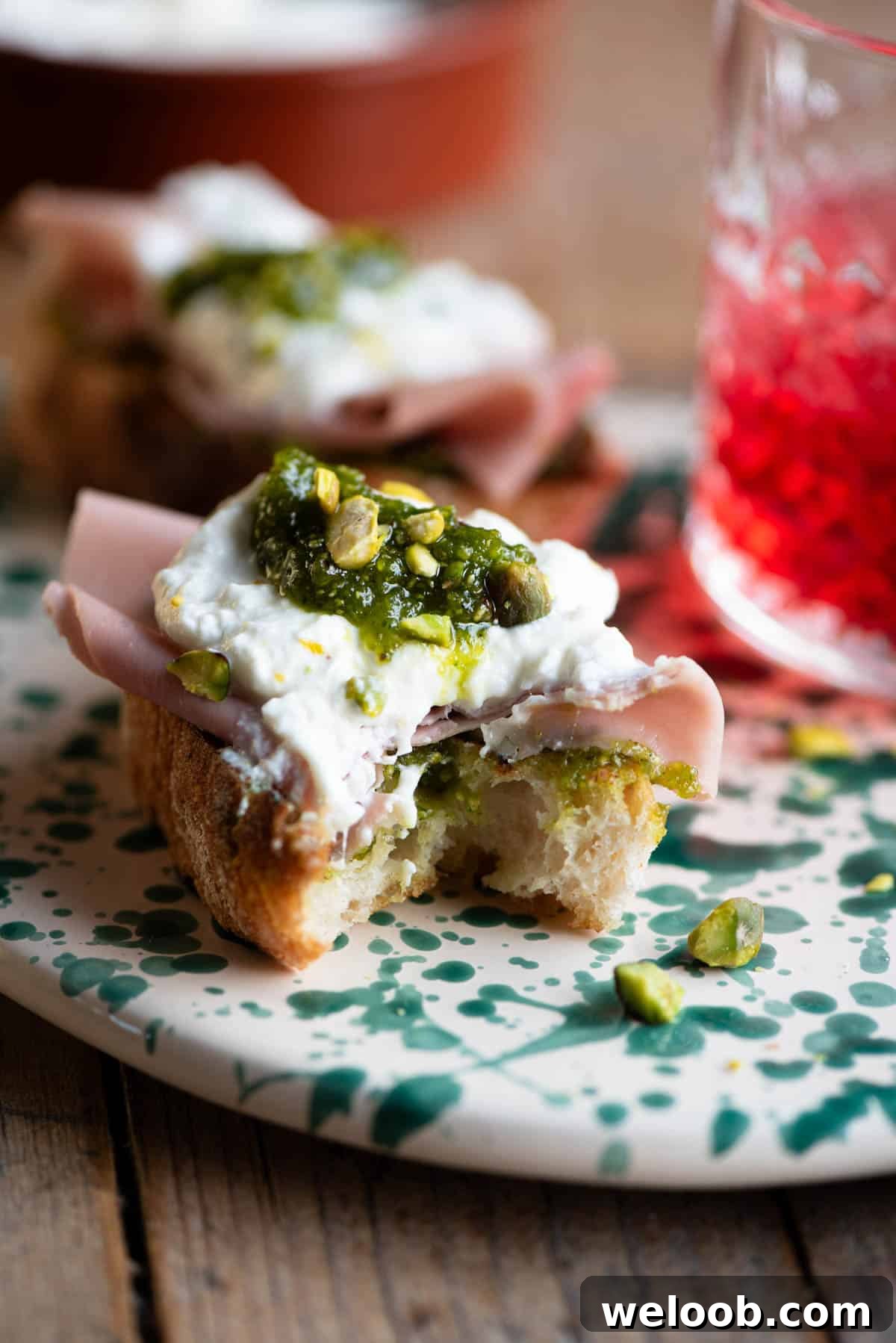 A close up of a mortadella, burrata and pistachio crostini with a bite out.