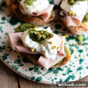 A close up cropped image of mortadella crostini with burrata and pistachios.