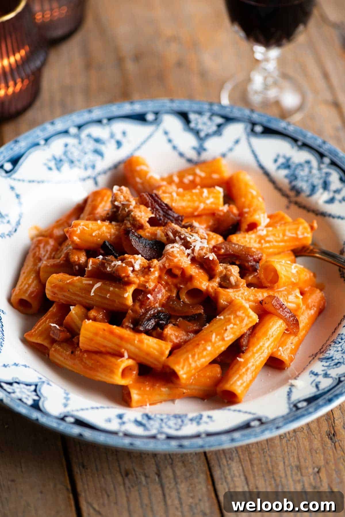 Rigatoni pasta with zozzona sauce in a blue and white patterned bowl sitting on a wooden table.