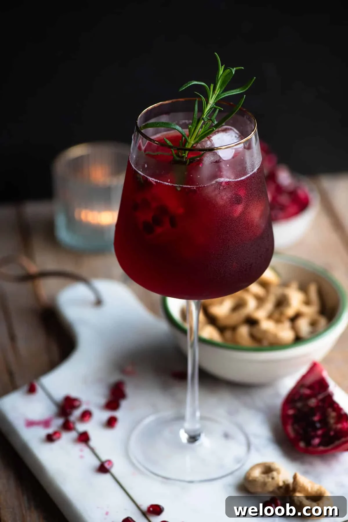 A pomegranate spritz in a tall wine glass with a gold rim and a sprig of rosemary inside.