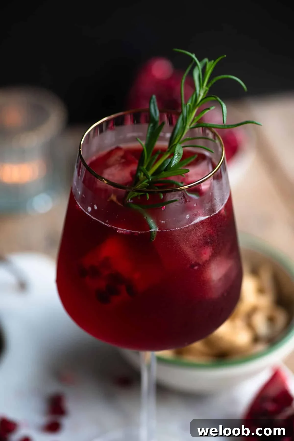A close up of a pomegranate spritz in a wine glass with a rosemary sprig.