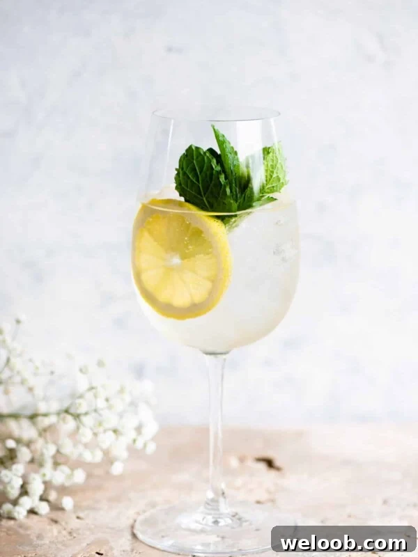 A Hugo spritz cocktail on a light coloured worktop with lemon and mint.