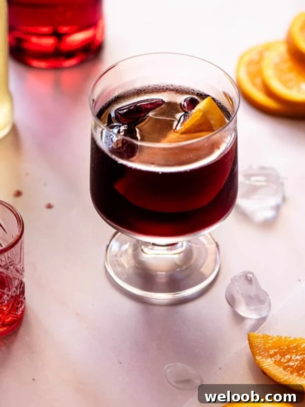 A red wine spritz (prampolini) on a light background with slices of orange, ice and campari at the side.