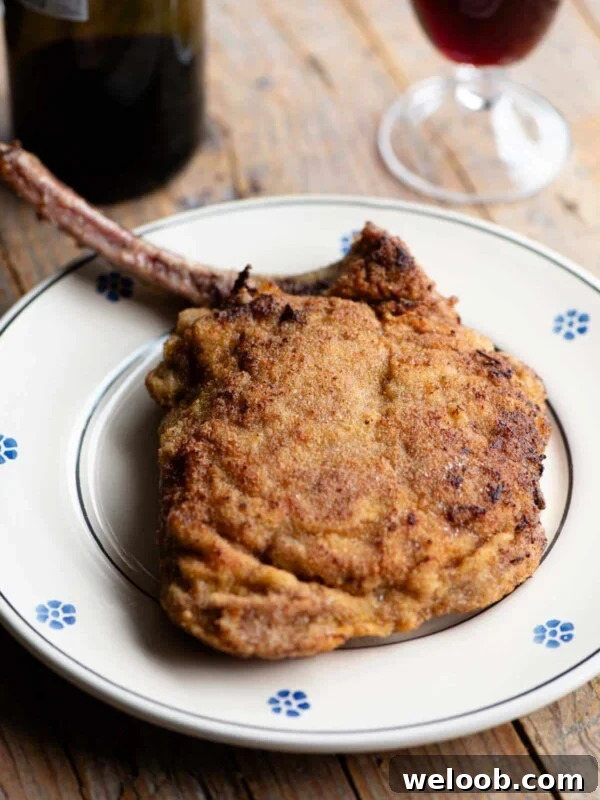 A breaded veal chop sitting on a plate with a glass and bottle of red wine in the background.