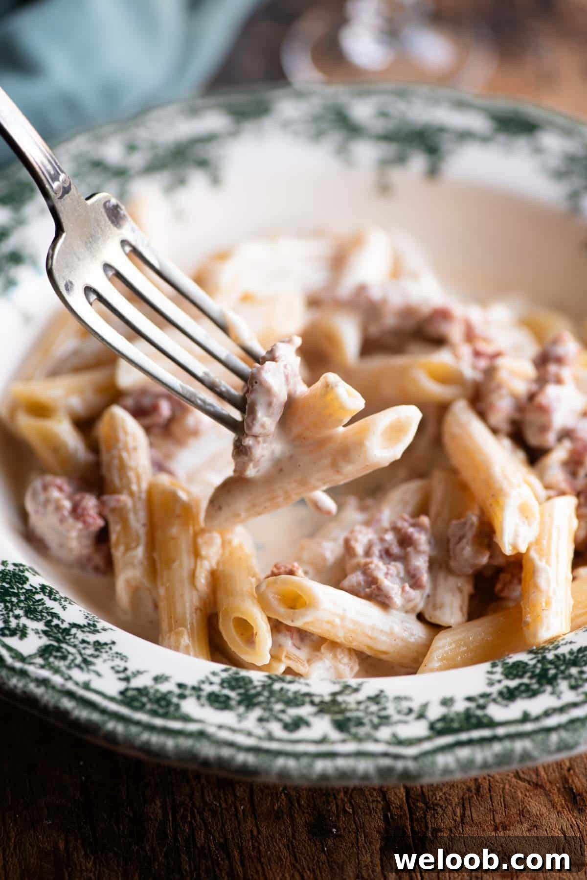 A close up of a fork picking up a bite of creamy sausage pasta.