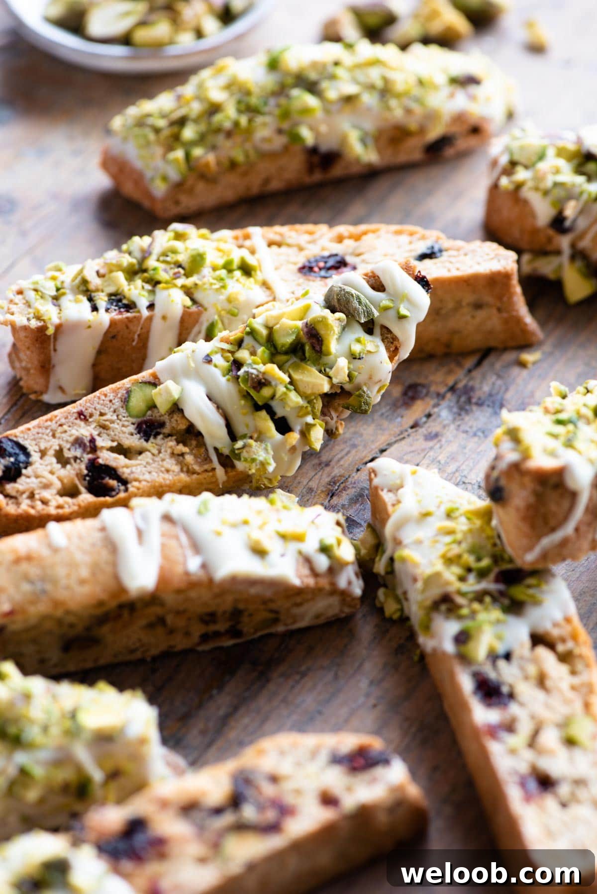 A close up of pistachio biscotti with cranberries and white chocolate on a wooden surface