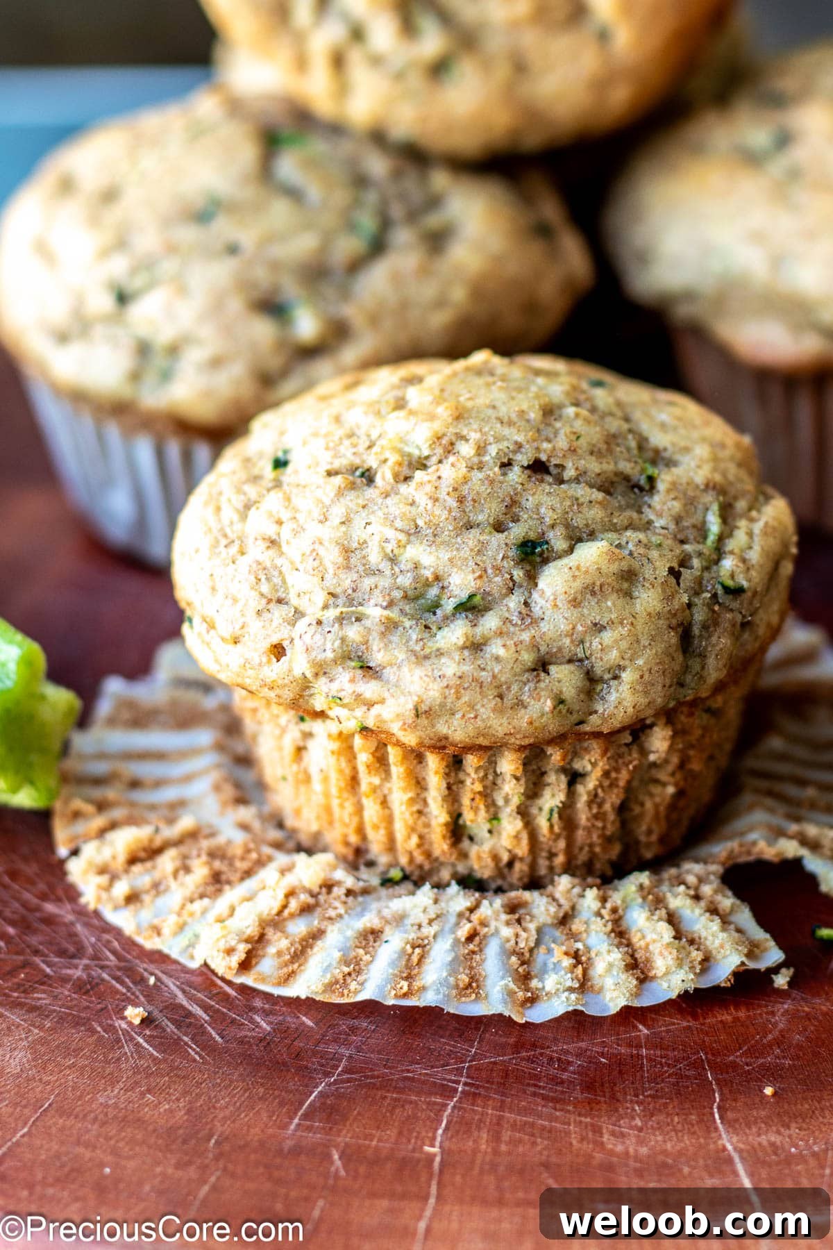 Zucchini muffin in foreground with paper lining peeled from it.