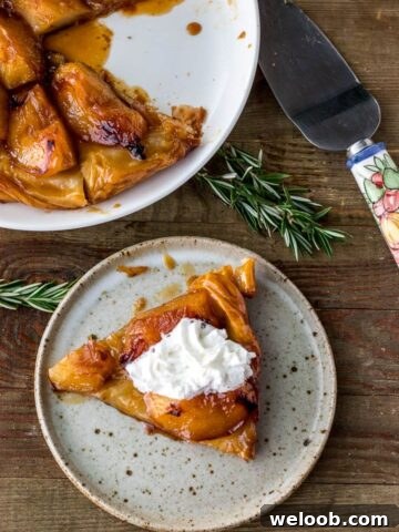 Slice of tarte tatin on a plate topped with cream, plate of large tarte tatin in the back