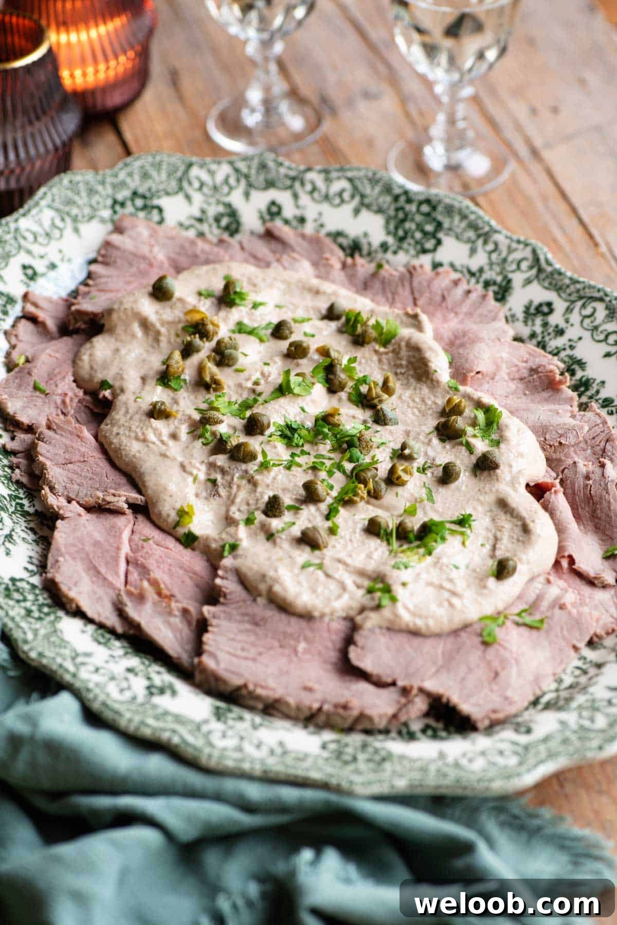 Vitello Tonnato on a serving platter topped with sauce, capers and parsley.