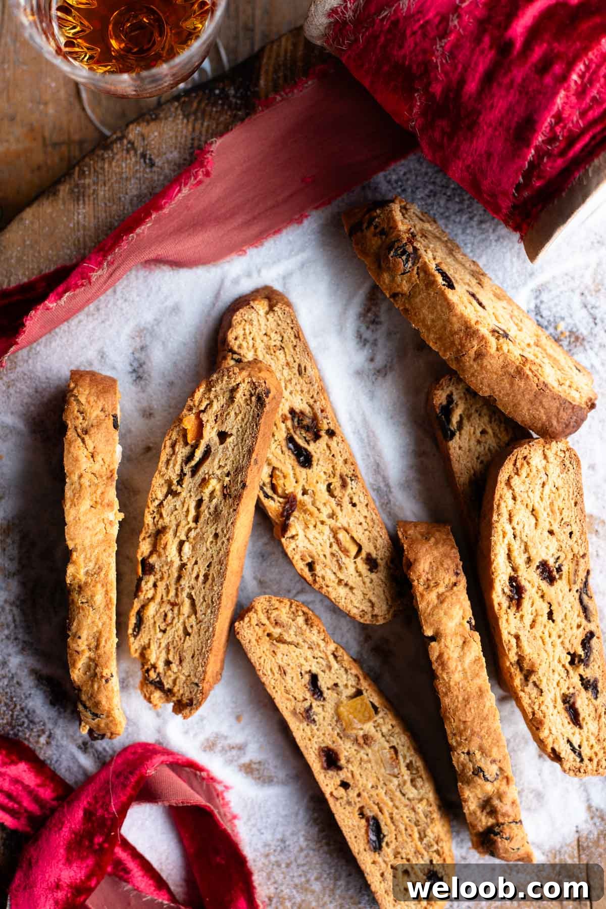 An overhead shot of panettone biscotti on a wooden surface with sugar and a red Christmas ribbon.