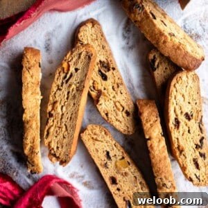A cropped square image of cantucci biscotti on a wooden surface dusted in sugar.