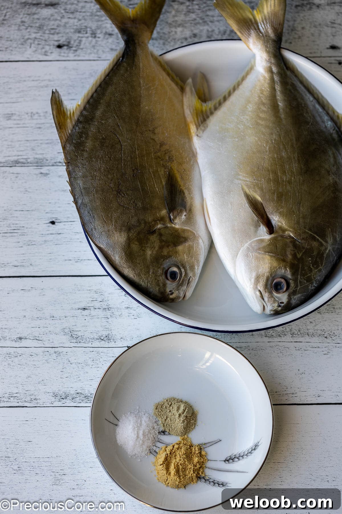 Njangsa Sauce Recipe from Cameroon: How to Make Authentic Njansa Stew 4 2 whole fish in a white bowl, a small plate with seasoning.