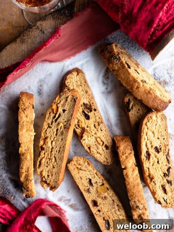 An overhead shot of panettone biscotti on a wooden surface with sugar and a red Christmas ribbon.