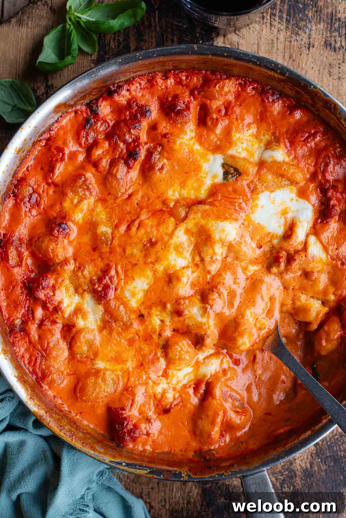 An overhead shot of spicy and creamy baked gnocchi in a skillet pan sitting on a wooden surface.