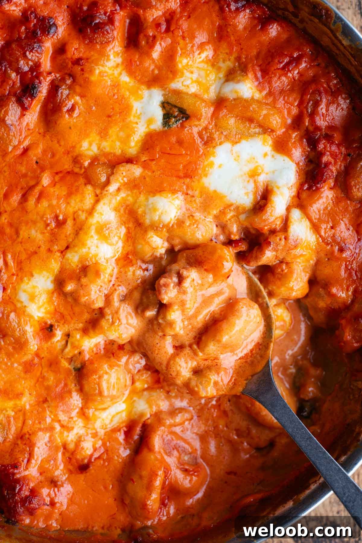 A close up of creamy baked gnocchi in a pan with a serving spoon.