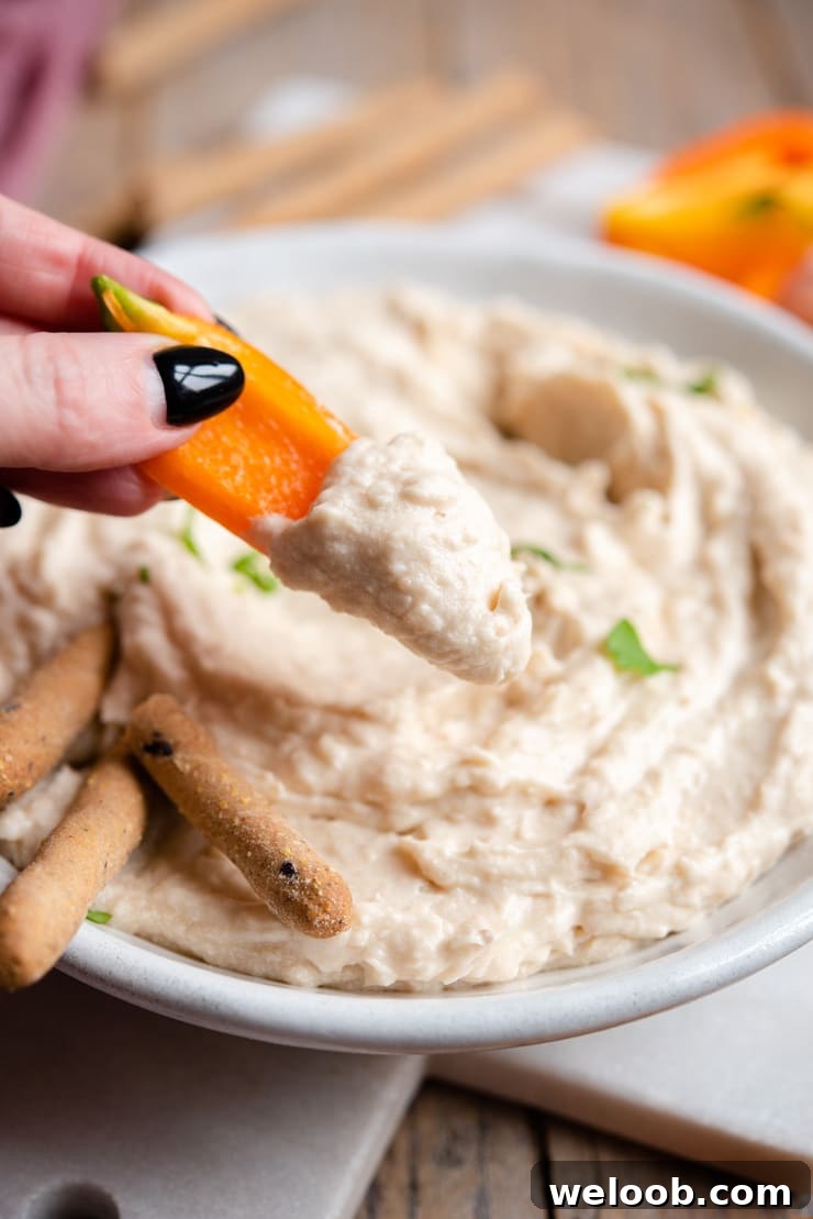 A close up of dipping bell peppers into a white bean dip
