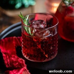 A close up cropped image of a red Italian cocktail in a short glass with a rosemary sprig.