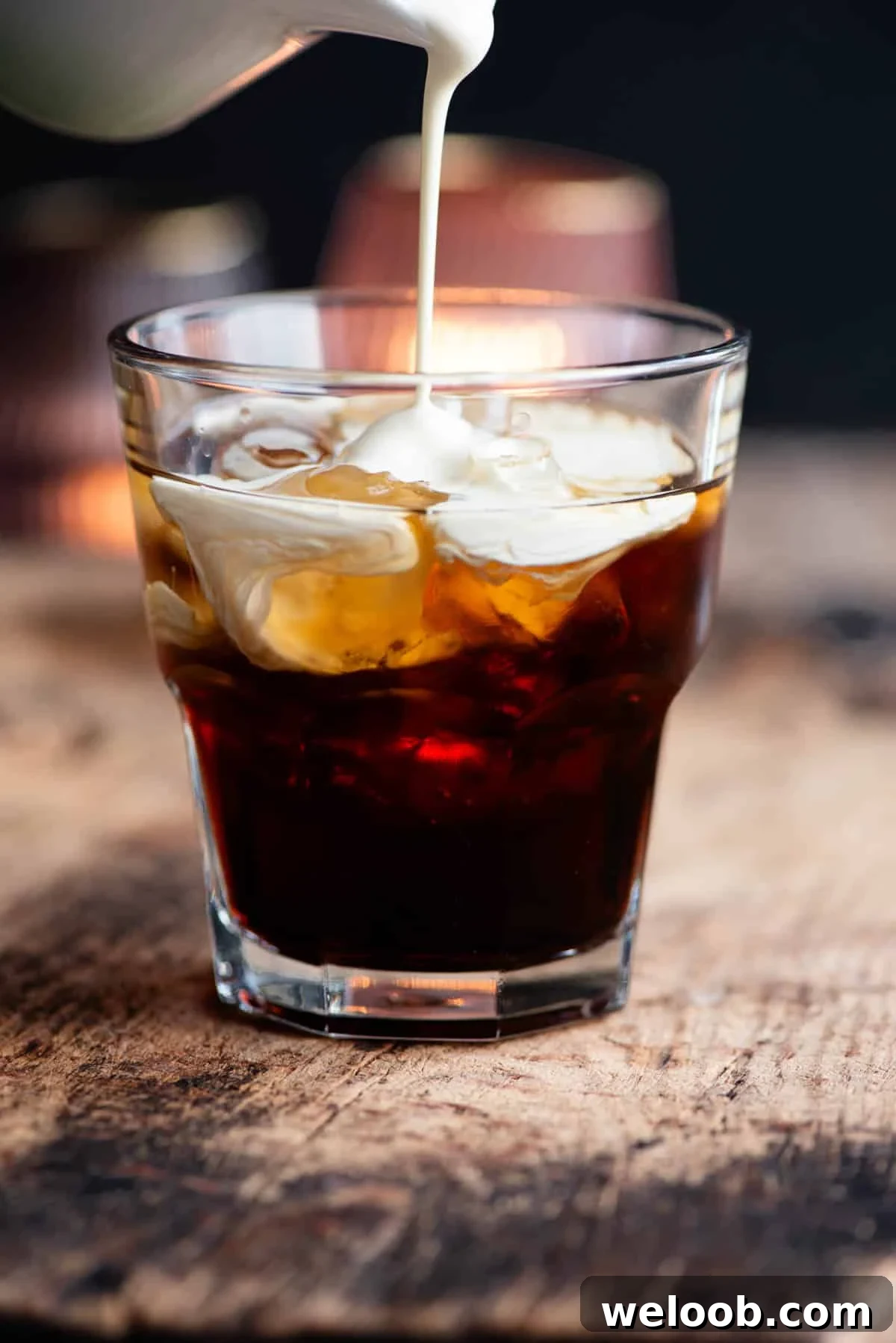 A close up of cream getting poured into a white russian cocktail.