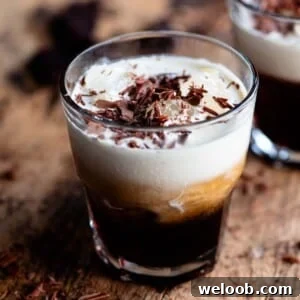 A close up cropped image of a white russian cocktail topped with chocolate shavings on a wooden table.