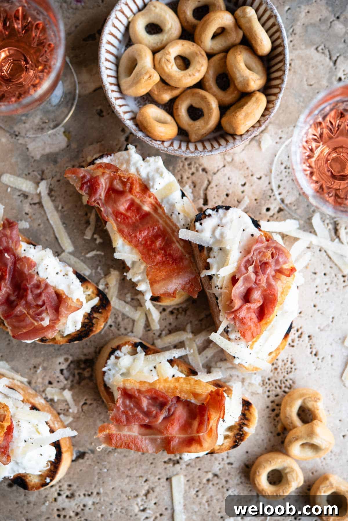 An overhead shot of burrata and Parmigiano crostini on a travertine background topped with prosciutto.