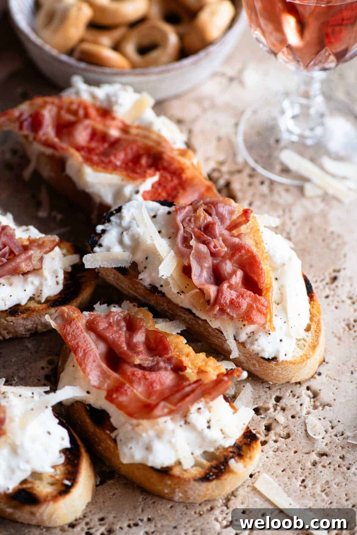 A close up of a slice of crostini topped with burrata, parmigiano reggiano and crispy prosciutto.