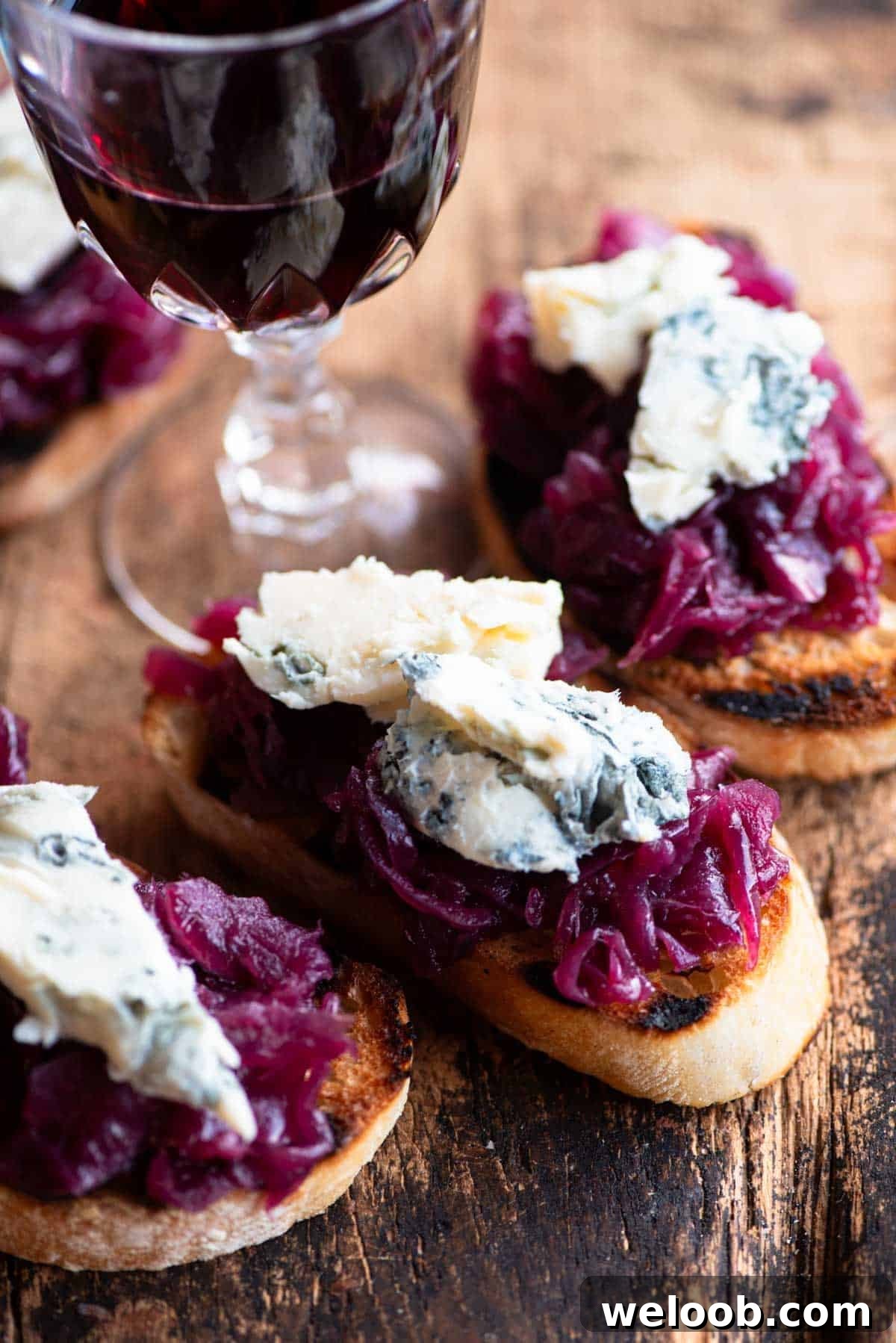 A close up of red onion and gorgonzola crostini on a wooden serving board.