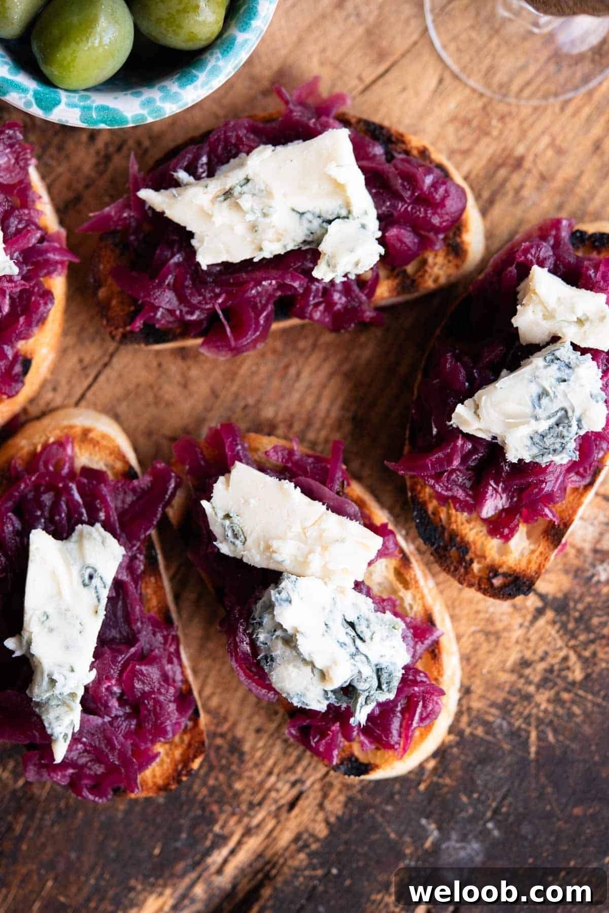 An overhead shot of red onion crostini topped with gorgonzola on a serving board.