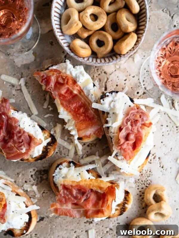 An overhead shot of burrata and Parmigiano crostini on a travertine background topped with prosciutto.