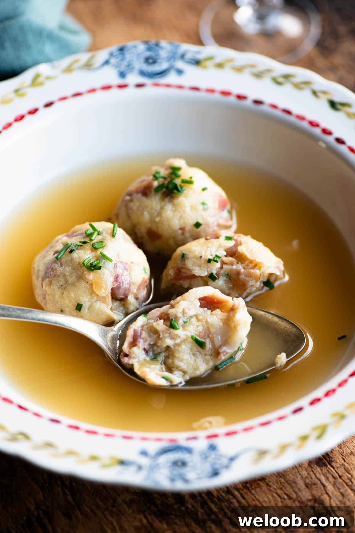 A side shot of canederli dumplings in broth with a spoons.
