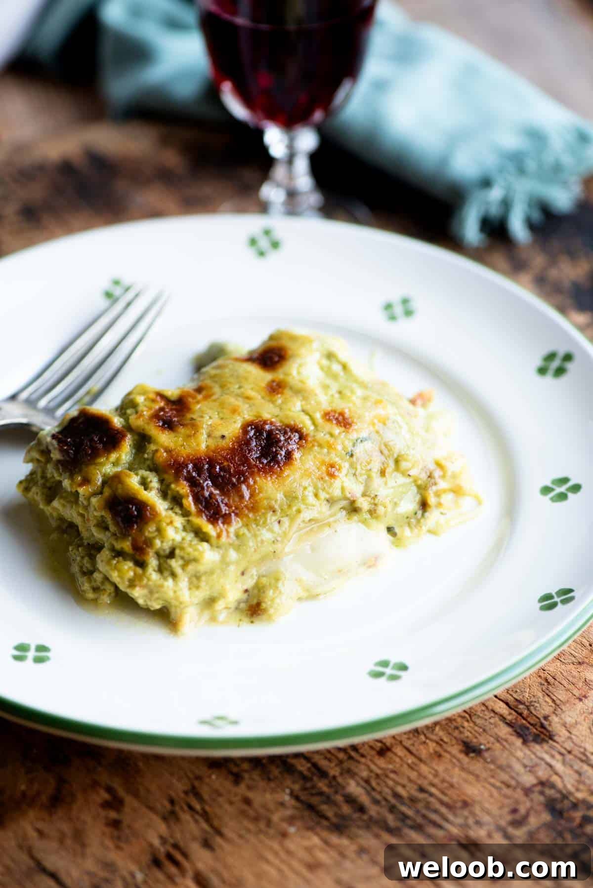 A slice of pistachio lasagna on a white plate with a fork at the side.