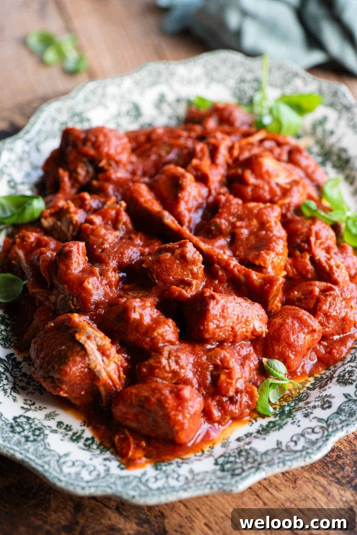 A side shot of lots of cooked meat in tomato sauce on a large serving plate.