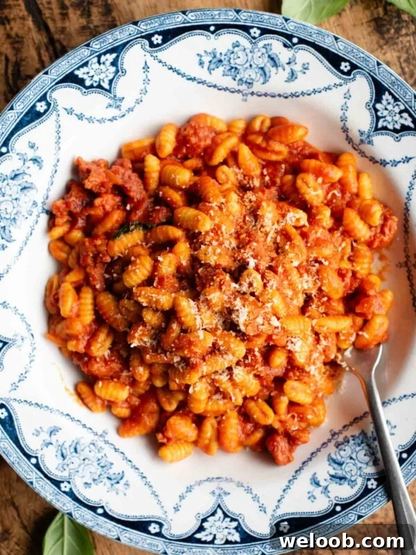An overhead shot of a Sardinian sausage ragu (Malloreddus alla Campidanese) in a blue and white bowl on a rustic wooden background.