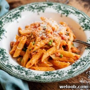A cropped square image of a bowl of creamy tomato penne pasta on a wooden table.