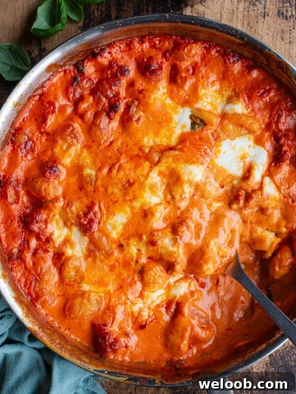 An overhead shot of spicy and creamy baked gnocchi in a skillet pan sitting on a wooden surface.