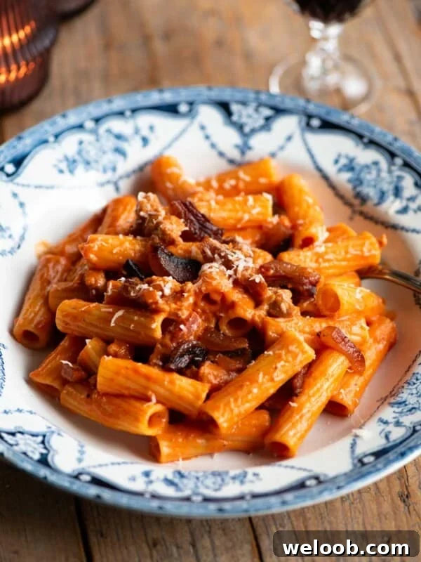 Rigatoni pasta with zozzona sauce in a blue and white patterned bowl sitting on a wooden table.