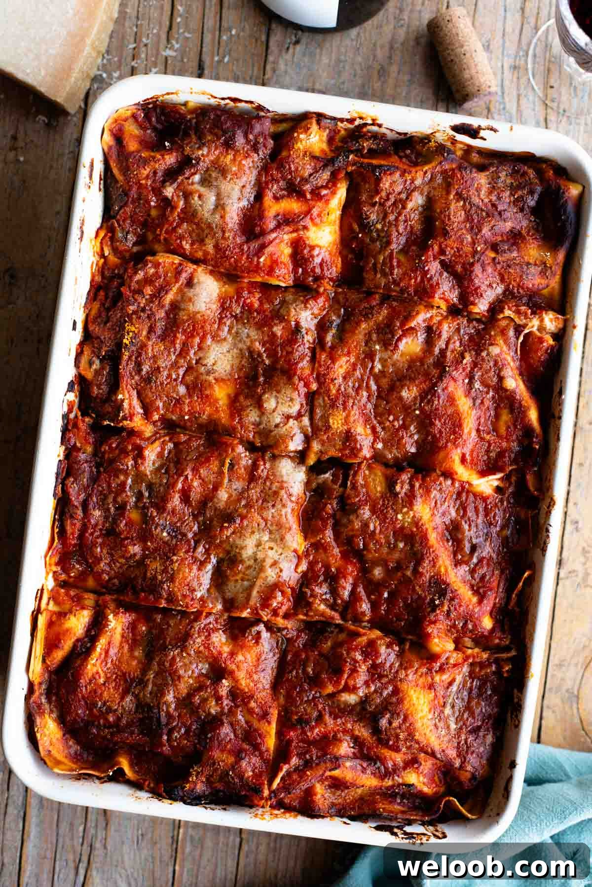An overhead shot of a Neapolitan lasagna sitting on a wooden table with a bottle of wine at the side.